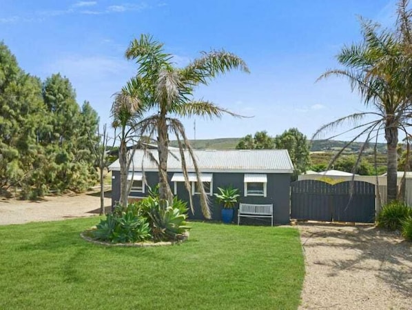 A single-story house with a metal roof, surrounded by a fenced yard with a well-maintained lawn and several palm trees.