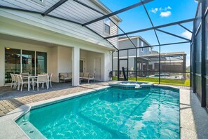 A swimming pool with a glass enclosure, a patio area with outdoor furniture, and a view of a residential neighborhood. - Windsor Resort 7BR Pool Home w/ Arcade Fun (Davenport)