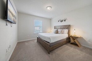 A bedroom with a bed, bedside table, wall-mounted TV, and a window with blinds.