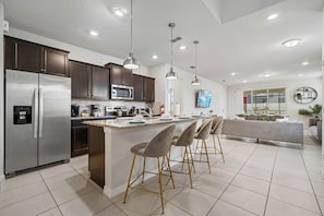 A modern kitchen with stainless steel appliances, a central island with bar stools, and pendant lighting.