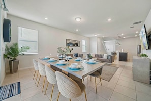 A modern dining area with a long table, chairs, and a central decorative piece. - Windsor Resort 7BR Pool Home w/ Arcade Fun (Davenport)