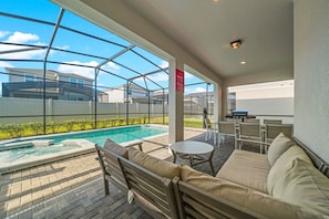 Et poolområde med en glasmuret patio, et opholdsområde med sofa og stole, samt et lille bord.