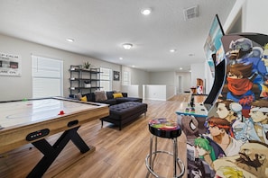 A modern living room with a pool table, a sofa, and a bar area with anime artwork. - Windsor Resort 7BR Pool Home w/ Arcade Fun (Davenport)