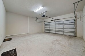 A garage with a single garage door, a ceiling-mounted projector, and a metal shelving unit against the wall.