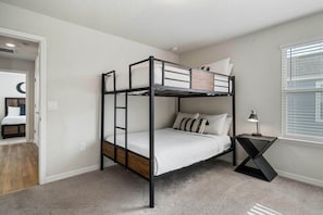 A bunk bed with a ladder, a bedside table with a lamp, and a window with blinds. - Windsor Resort 7BR Pool Home w/ Arcade Fun (Davenport)