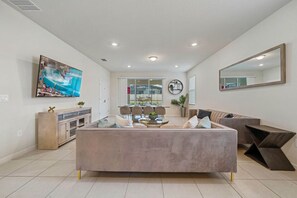 A modern living room with a central sofa, a coffee table, and a TV mounted on the wall. - Windsor Resort 7BR Pool Home w/ Arcade Fun (Davenport)