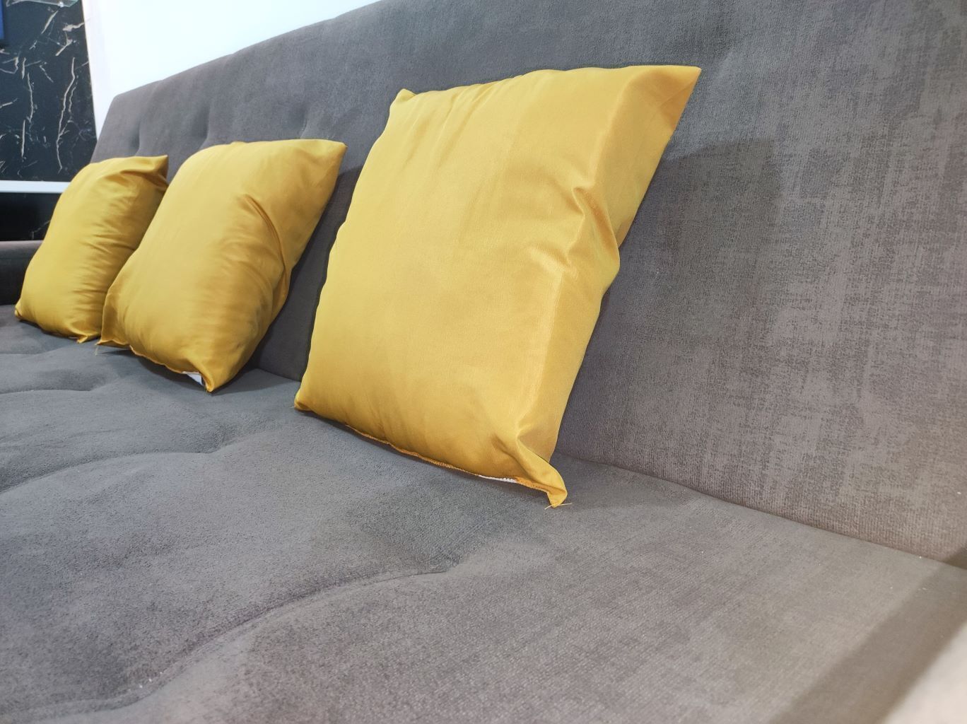 A grey sofa with two yellow pillows.