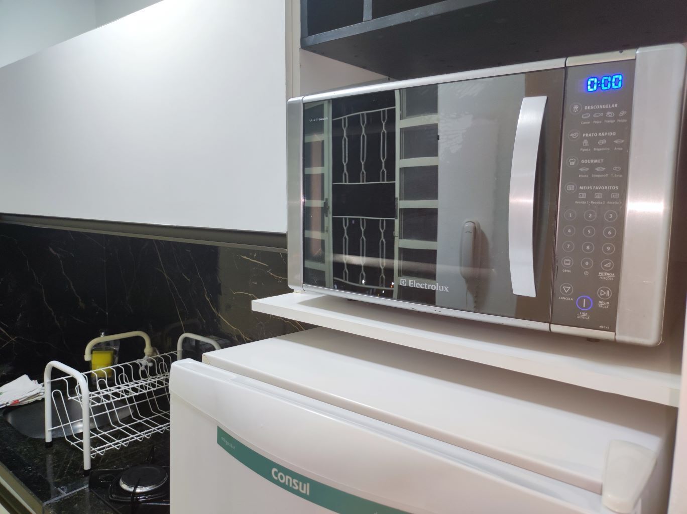 A modern kitchen with a microwave on top of a white refrigerator.