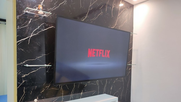 Una TV a schermo piatto montata su una parete di marmo nero con uno scaffale bianco sottostante.