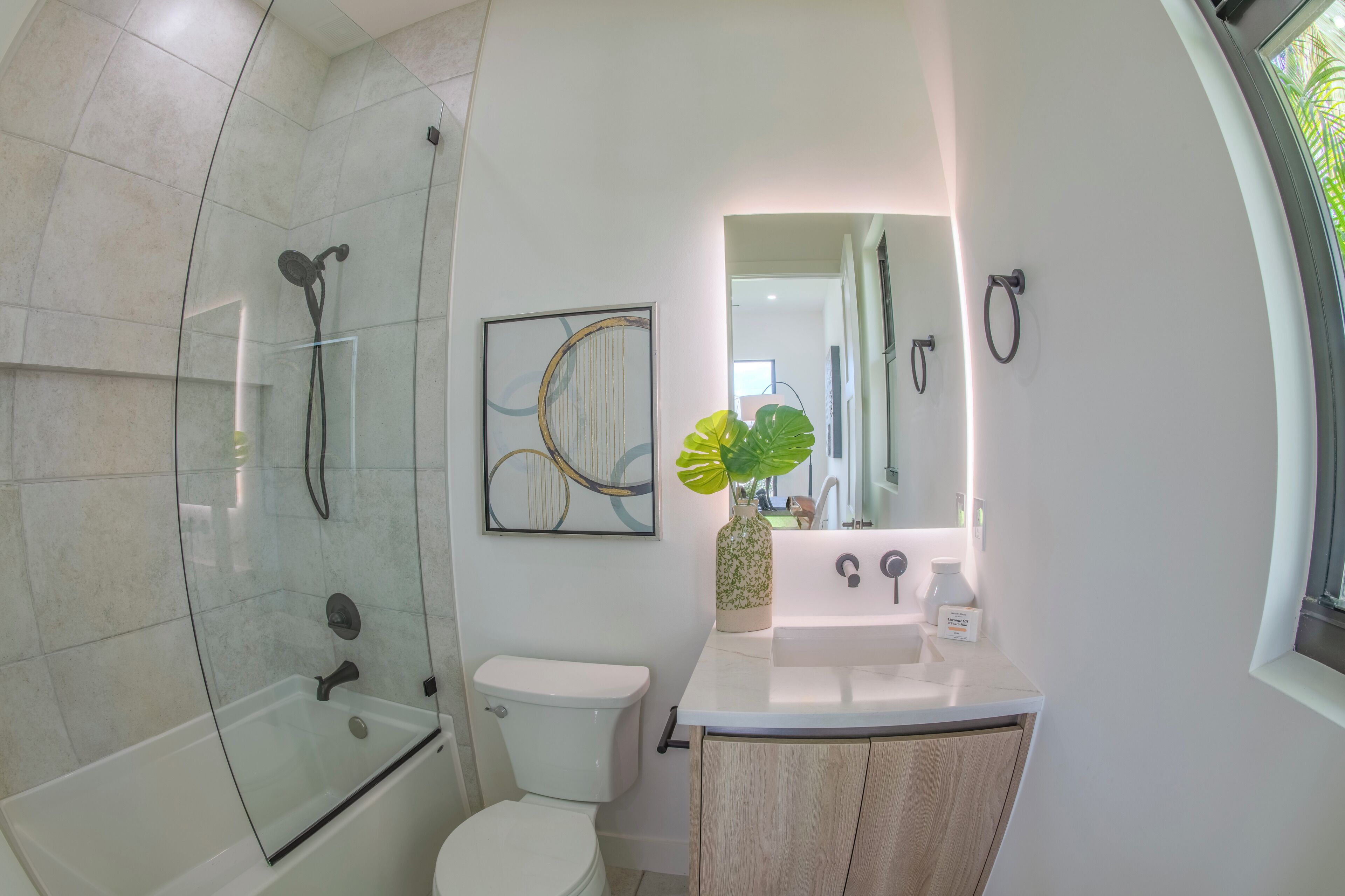 A modern bathroom with a glass-enclosed shower, a toilet, a sink with a mirror, and a potted plant.