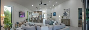 A modern living room with a grey sofa, a dining area with white chairs, and a kitchen in the background. - New Construction, 5 Bedroom, 4.5 Bathroom, Pool and Spa. Sleeps 12! (Naples)