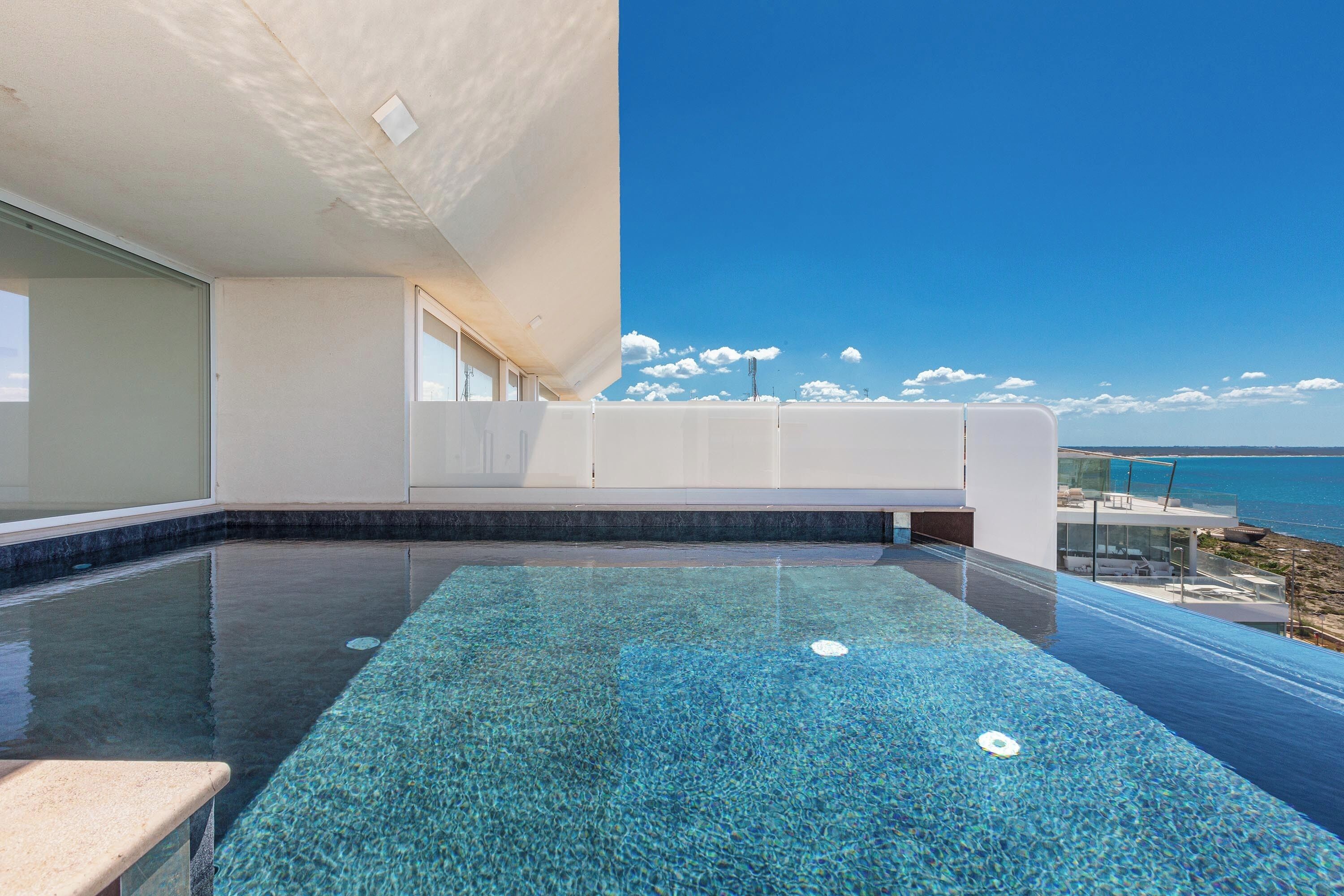 Una piscina infinita moderna con vistas despejadas al océano y un edificio blanco con grandes ventanales.