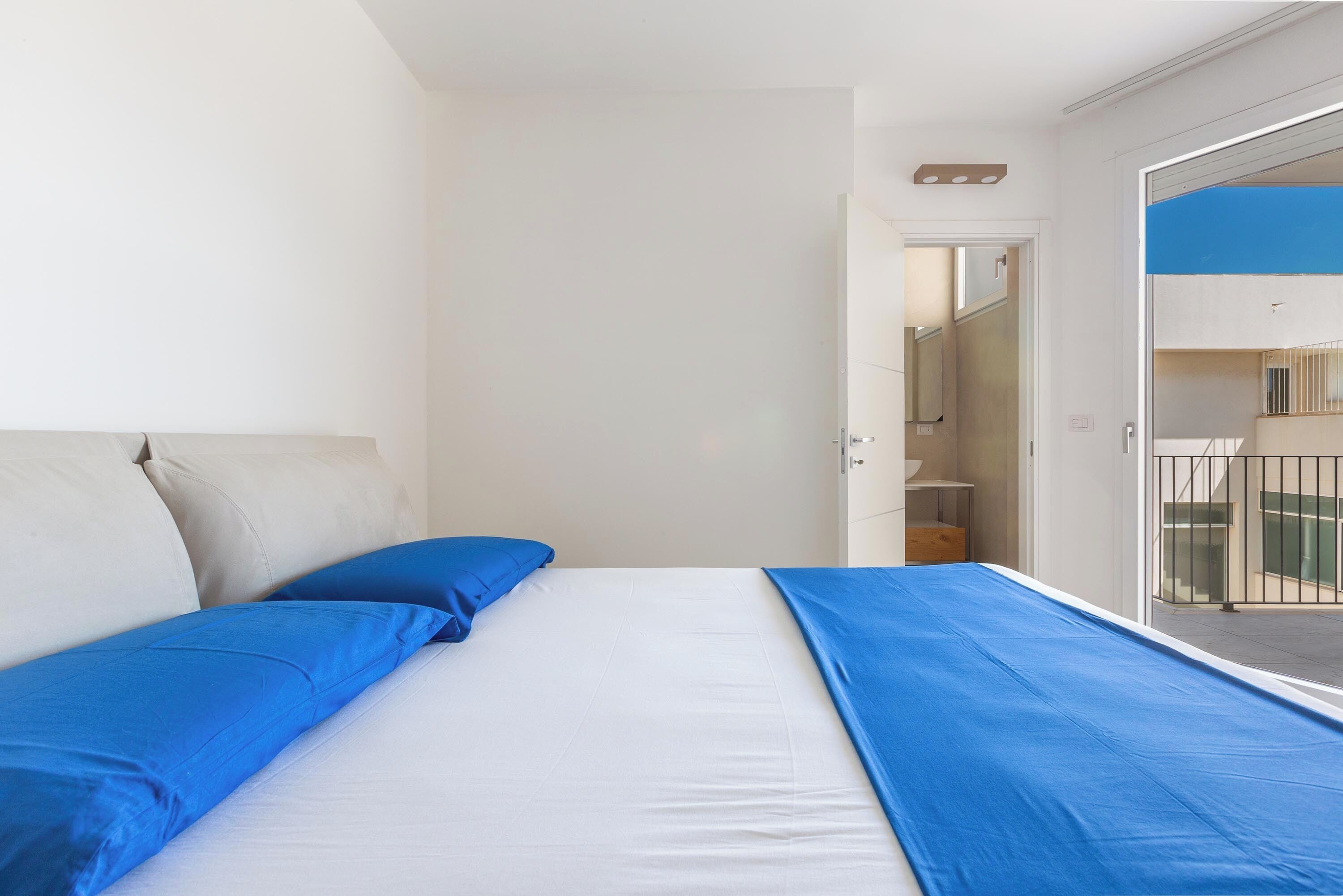 A bedroom with a bed, a door leading to a balcony, and a white wall.