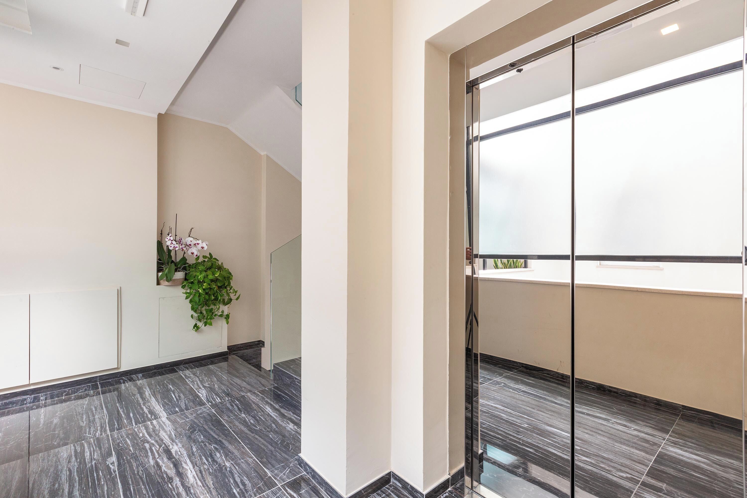 Ein modernes Interieur mit Marmorboden, einer Topfpflanze und einer Glastür, die auf einen Balkon führt.