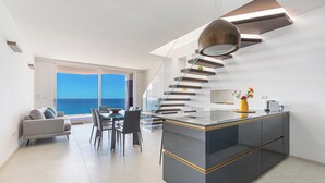 A modern kitchen with a central island, a dining area with a view of the sea, and a staircase leading to an upper level. - 4009 Attico Smeraldo by Perle di Puglia (Gallipoli)