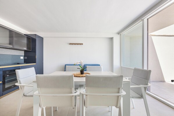 A modern kitchen with dark blue cabinets, a white dining table, and four white chairs. - 4009 Attico Smeraldo by Perle di Puglia (Gallipoli)
