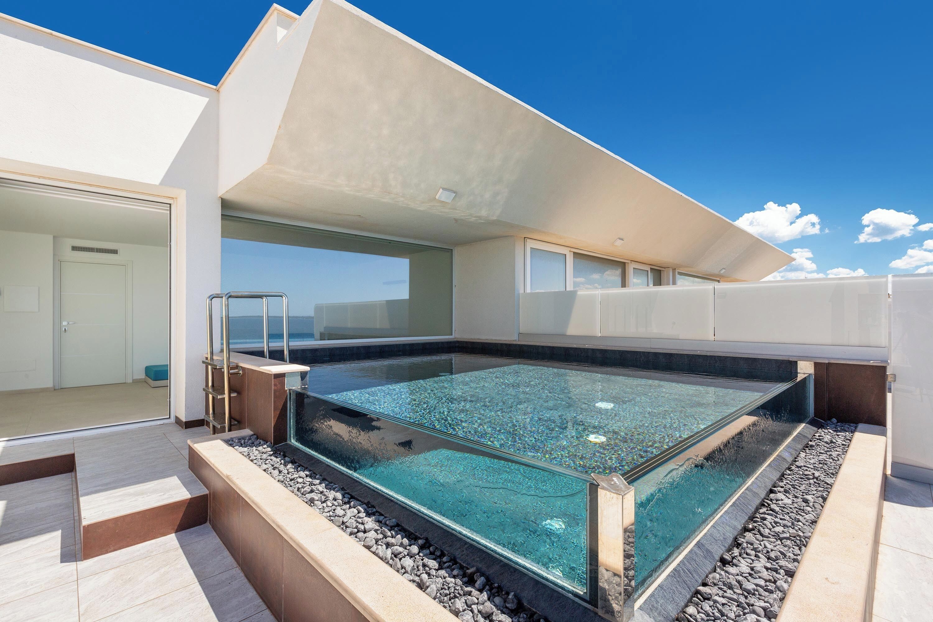 Una piscina moderna al aire libre con agua cristalina, rodeada por una solana con revestimiento de guijarros y un diseño arquitectónico minimalista.