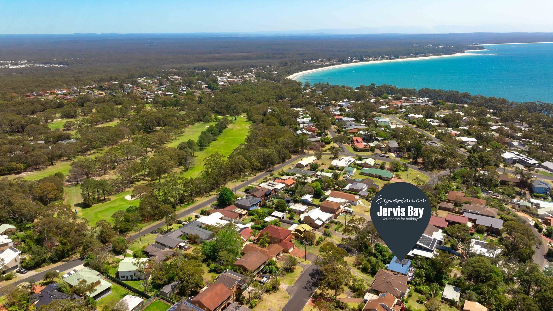 An aerial view of a residential area with houses, green spaces, and a beach.