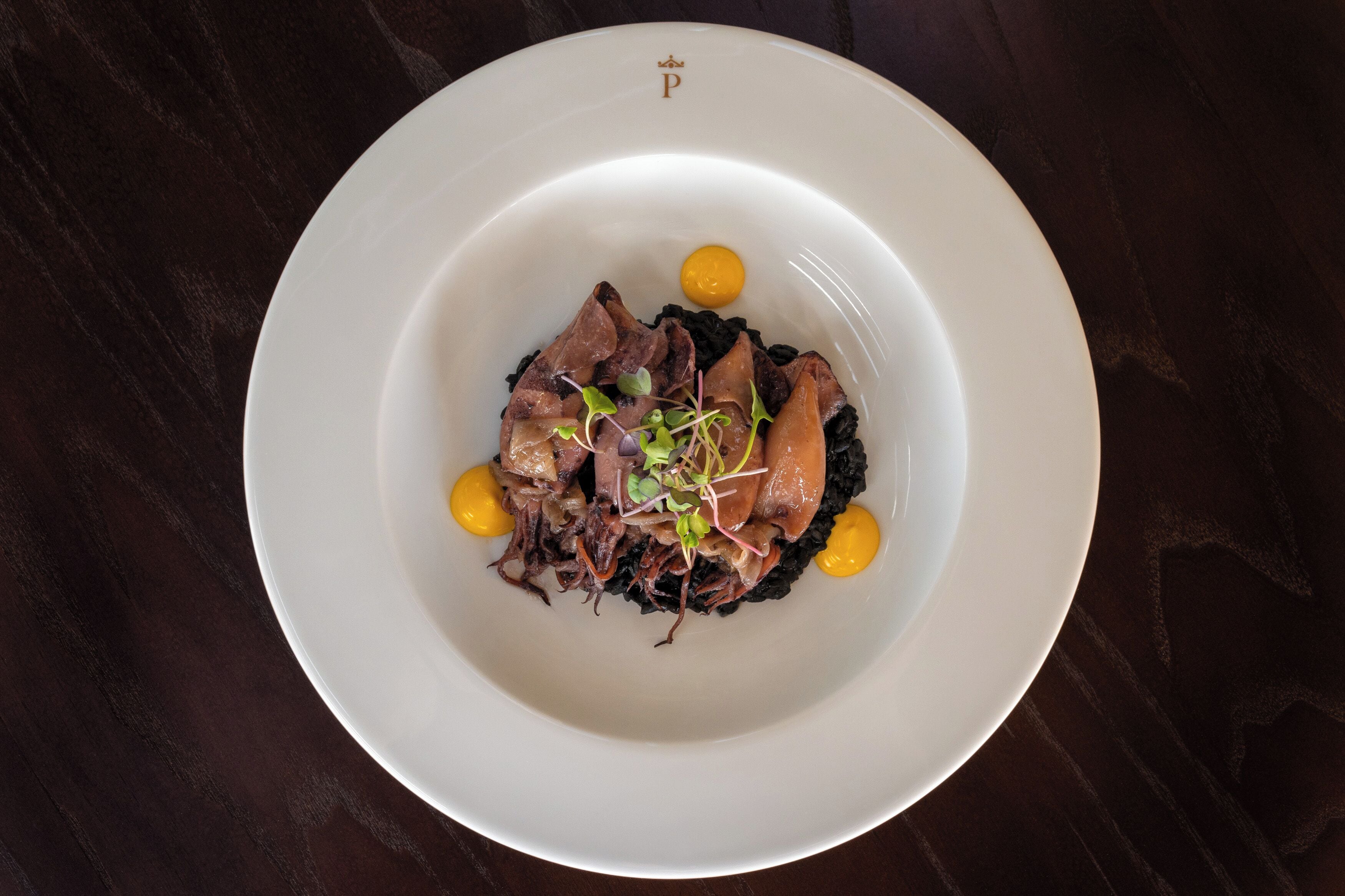 Un plato blanco con guiso de carne y vegetales sobre una mesa de madera oscura.