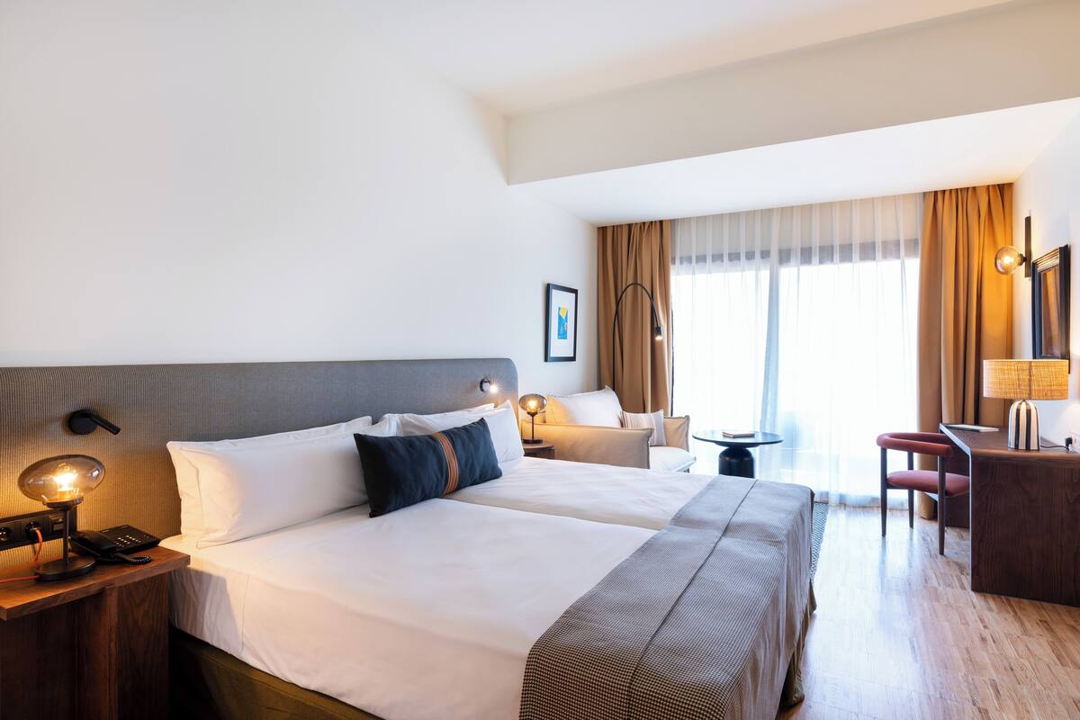 Habitación de hotel con dos camas, un escritorio, una silla, una lámpara y una mesita de noche con teléfono y control remoto.