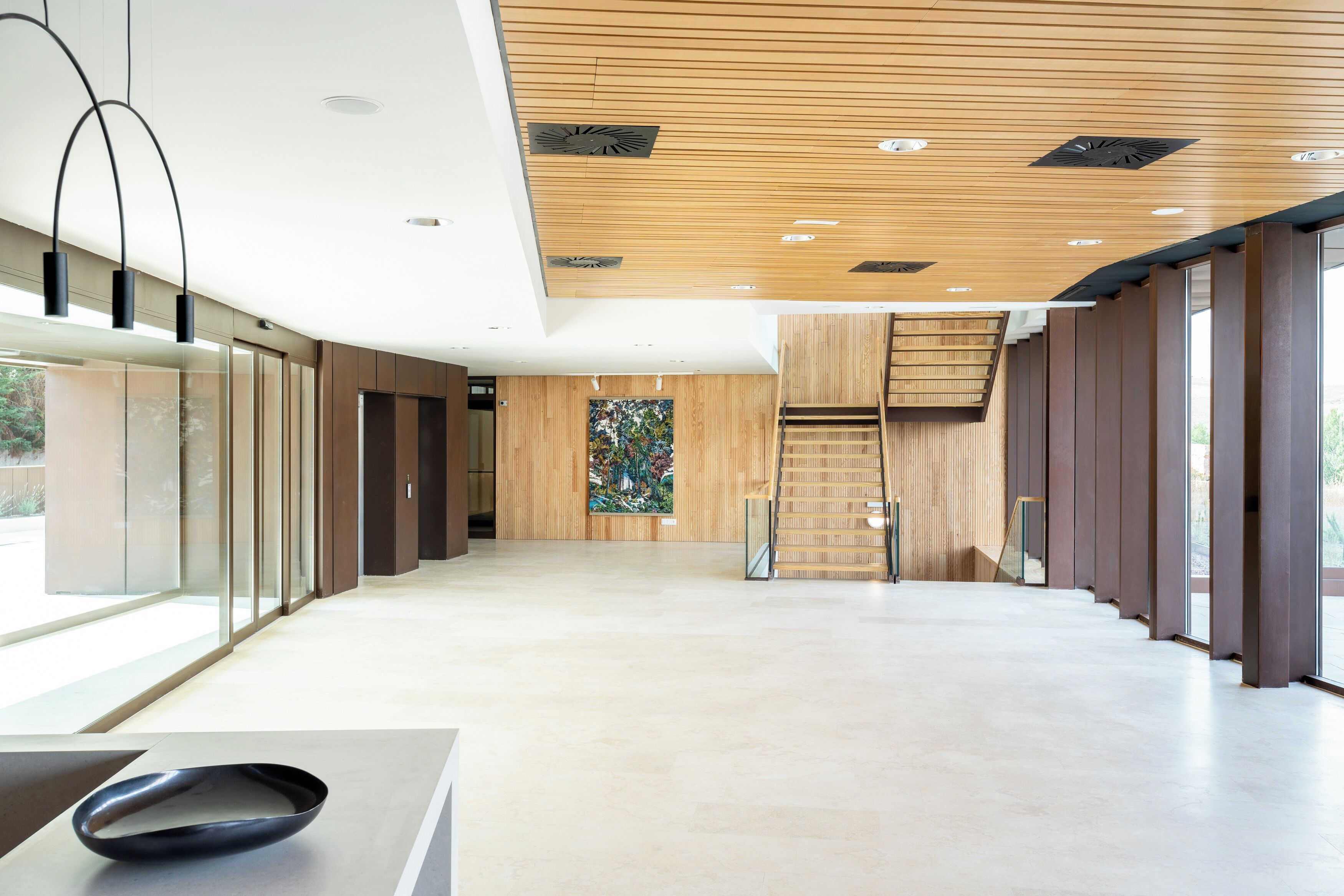A spacious lobby with a wooden ceiling, a staircase, and a large window.