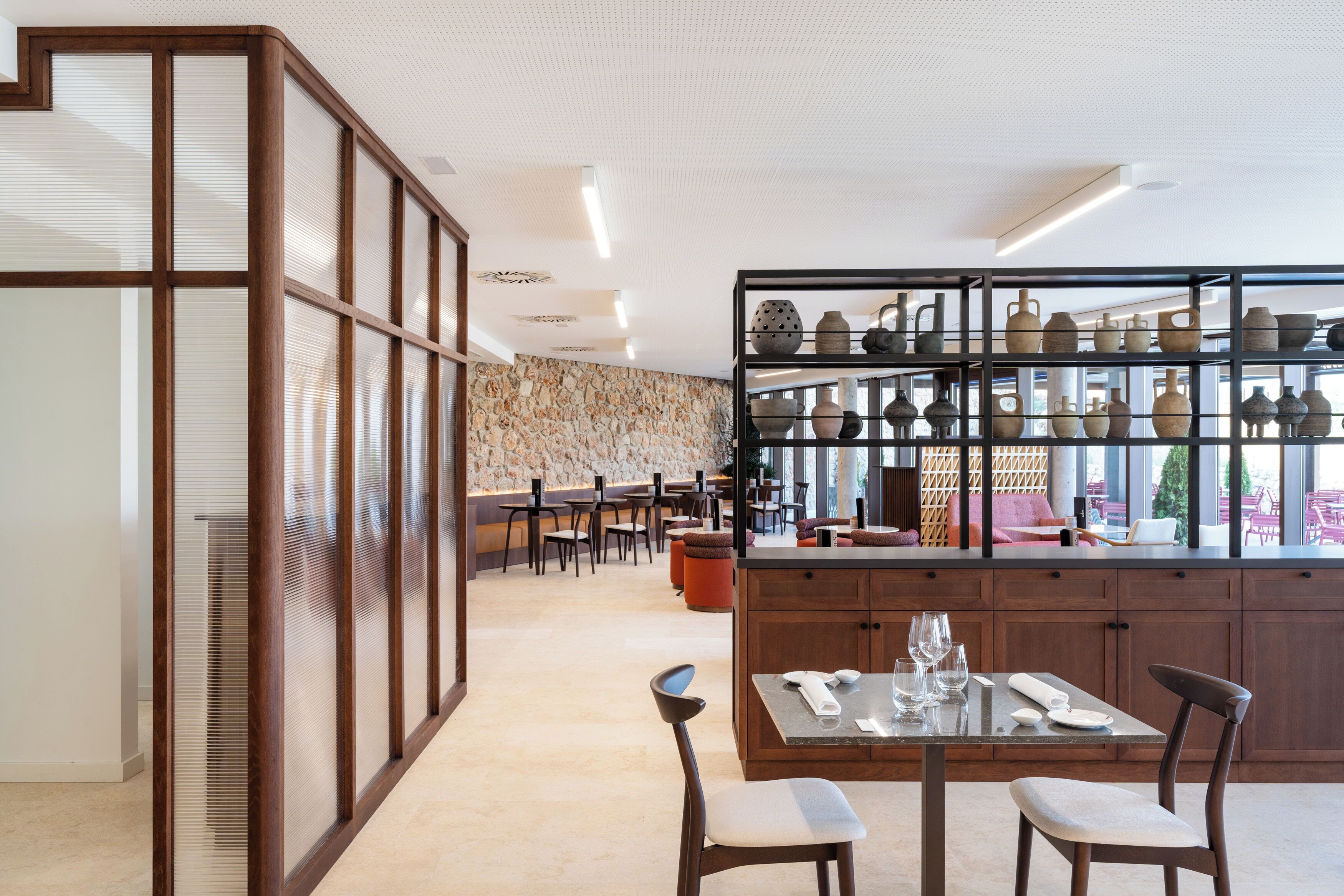 A restaurant with a long counter, wooden chairs, and a display of pottery on shelves.