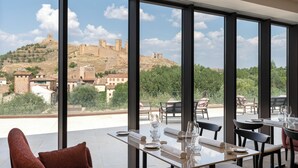 Comedor con una mesa dispuesta para dos personas, ventanas amplias que ofrecen vistas a una antigua fortaleza en la cima de una colina.