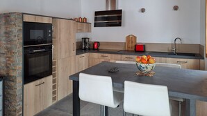 A modern kitchen with wooden cabinets, a built-in oven, a coffee maker, and a bowl of fruit on the table. - Chalet Briançon Serre Chevalier (Briançon)