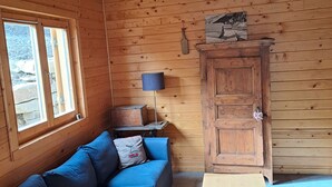 A cozy cabin interior with a wooden ceiling, a blue sofa, a small table, and a cabinet. - Chalet Briançon Serre Chevalier (Briançon)