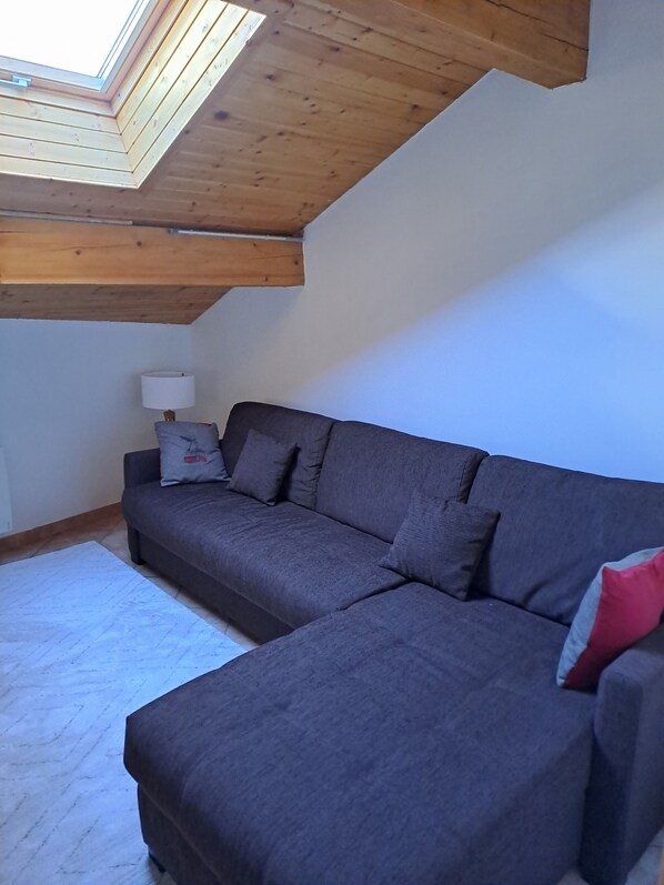 Une pièce avec un plafond en bois, un canapé gris, une lampe blanche et un tapis blanc.