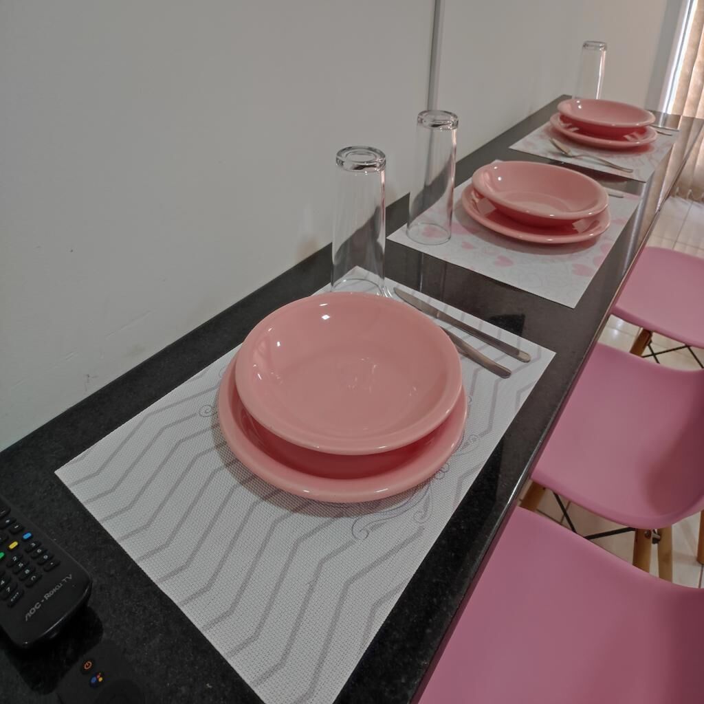 Un comedor con platos y cubiertos rosas sobre una mesa, un control remoto y un espejo que refleja la escena.