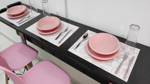 Un comedor con sillas rosadas y platos, una mesa negra y una botella de vidrio.