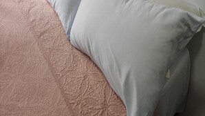 Una cama con un edredón rosa y dos almohadas blancas frente a una pared lisa.