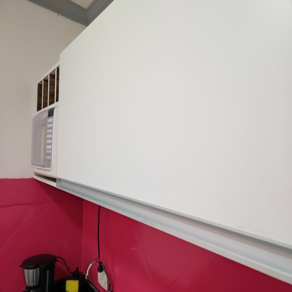 Uma cozinha com um micro-ondas branco, uma cafeteira e uma parede vermelha.
