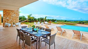 An outdoor dining area with a stone wall, wicker chairs, and a view of the ocean.