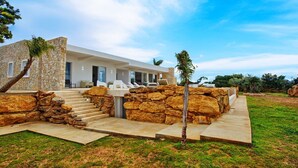A modern house with a stone facade, a staircase leading to a covered porch, and outdoor seating.