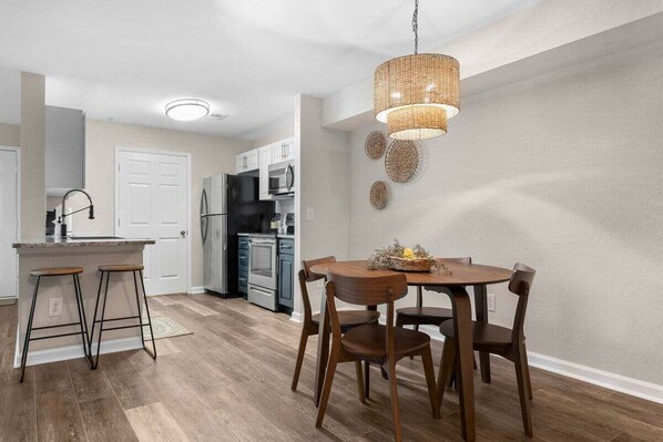 Una cocina moderna con comedor, que incluye una mesa redonda de madera, cuatro sillas y una lámpara colgante.
