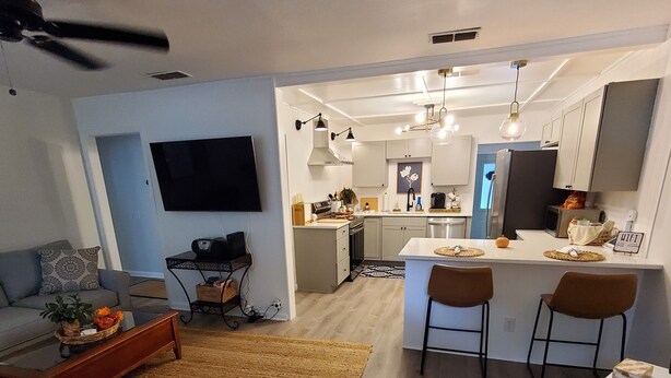 A modern living room with a sofa, coffee table, and a TV. There's a kitchen area with a dining table and chairs.