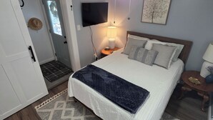 A bedroom with a bed, a ceiling fan, a TV, a bedside table, and a door.