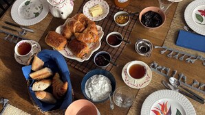 A breakfast table set with croissants, fruits, and beverages, surrounded by plates, cups, and utensils. - Auberge des Hirondelles (Puycelci)
