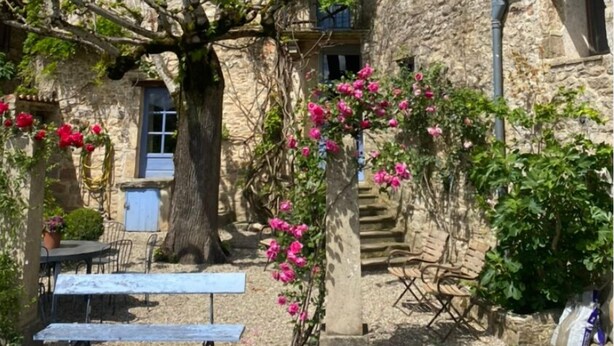 A stone building with multiple windows and a tree in the courtyard. - Auberge des Hirondelles (Puycelci)