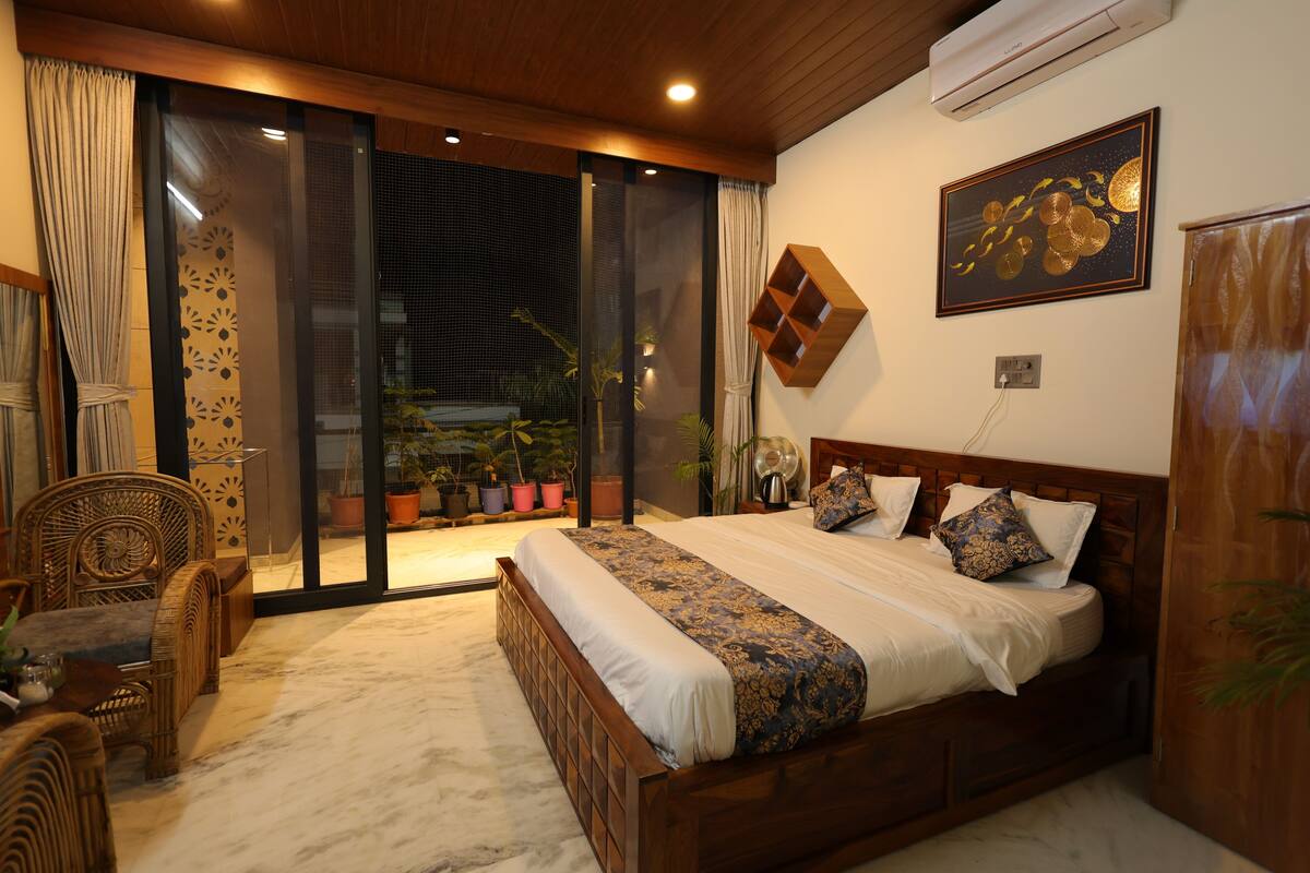 A bedroom with a large bed, a wooden headboard, and a sliding glass door leading to a balcony with potted plants.
