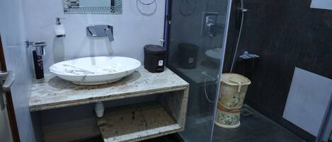 Casa de banho com lavatório branco, espelho, cabine de duche em vidro e um contentor de lixo.
