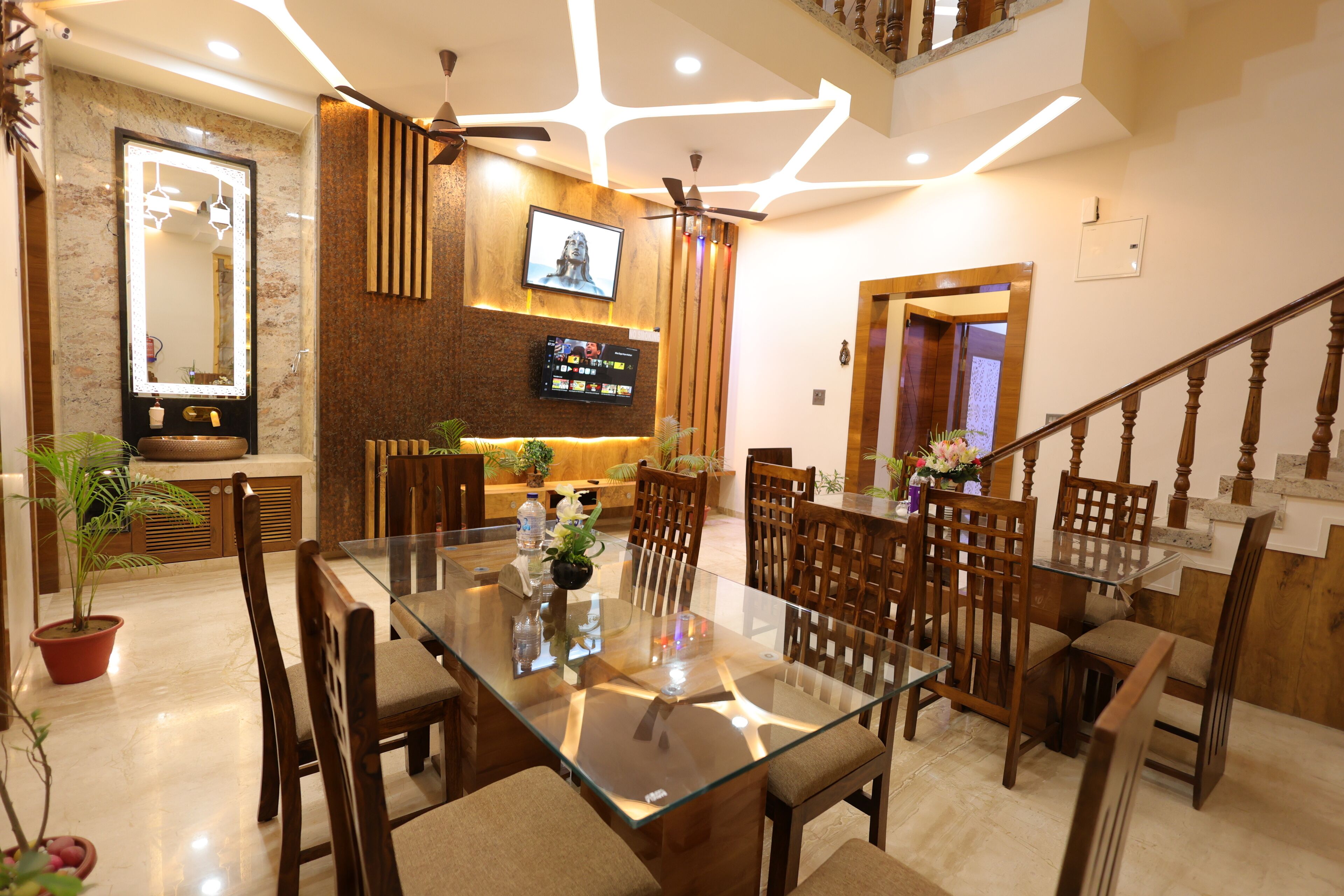 Uma sala de jantar moderna com mesa de vidro, cadeiras de madeira e televisão na parede.