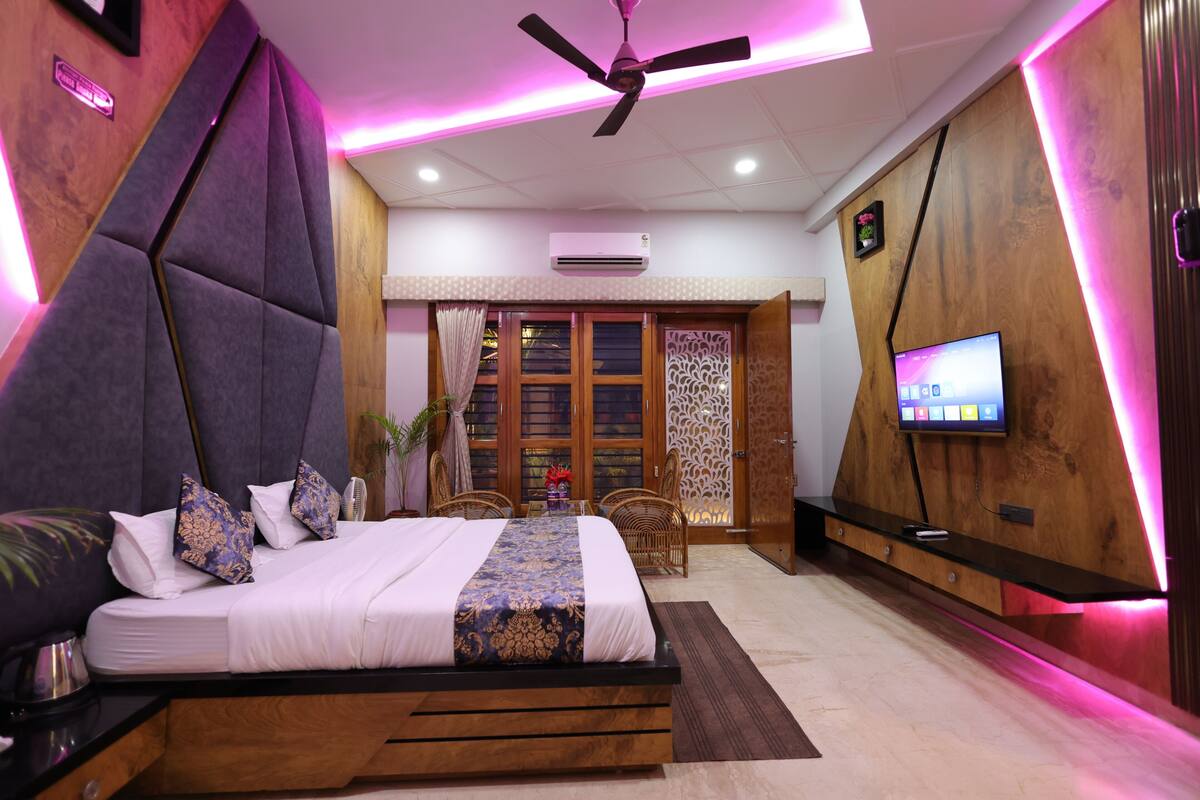 A modern bedroom with a bed, a ceiling fan, a TV, and a wooden accent wall.