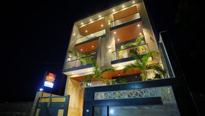 A multi-story hotel with a modern design, featuring balconies and a well-lit facade. - Amritam Palace A Luxury AC Home Stay (Shri Madhopur)