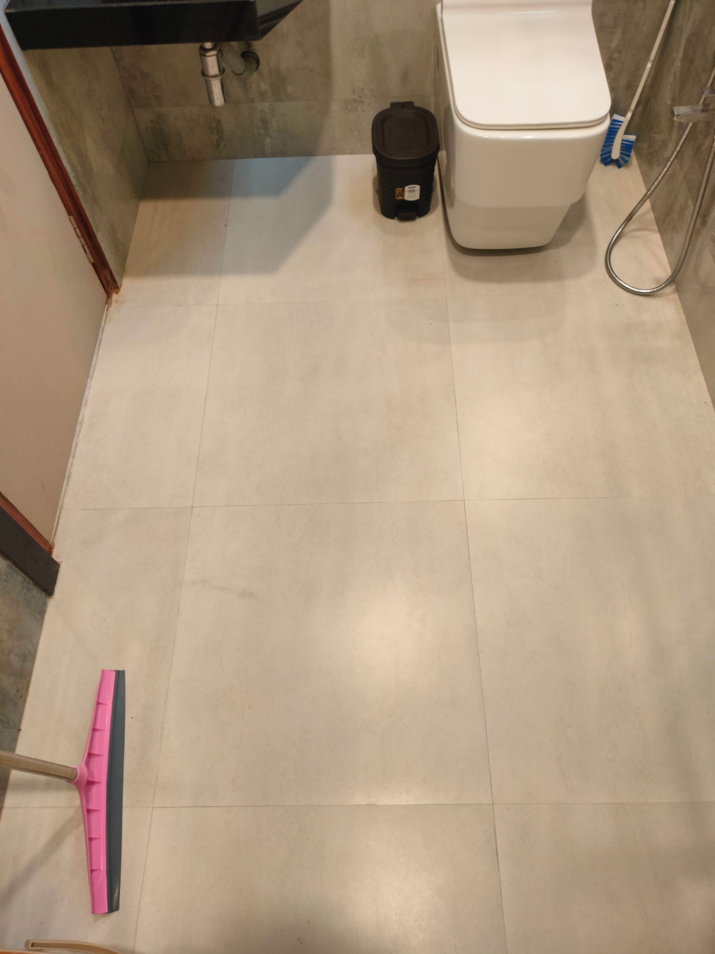 A bathroom with a toilet, a trash bin, and a cleaning tool on the floor.