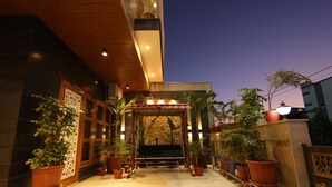 An outdoor entrance with a wooden swing, potted plants, and a stone wall. - Amritam Palace A Luxury AC Home Stay (Shri Madhopur)