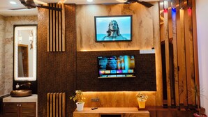 A modern bathroom with a wooden vanity, a large mirror, a television mounted on the wall, and ceiling fans. - Amritam Palace A Luxury AC Home Stay (Shri Madhopur)