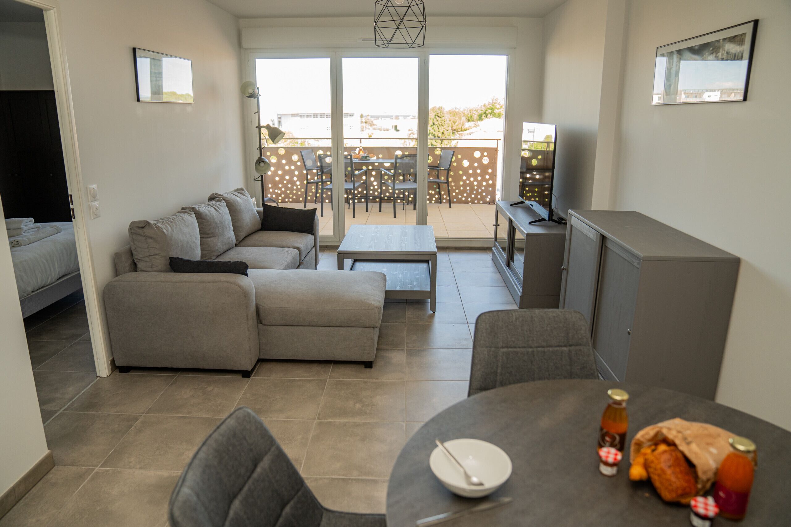 A modern living room with a sofa, a dining table with a bottle, and a TV.